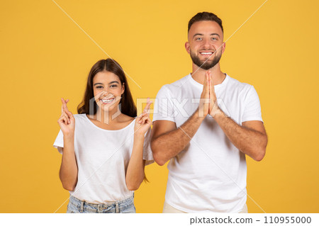 Smiling young european man and woman in white t-shirts with crossed fingers hoping or wishing Smiling young european man and woman in white t-shirts with crossed fingers hoping or wishing 110955000