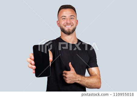 Glad strong young caucasian man with beard, show smartphone with empty screen and thumb up gesture with hand 110955018