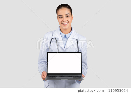 Cheerful caucasian young woman doctor in white coat show laptop computer with blank screen 110955024