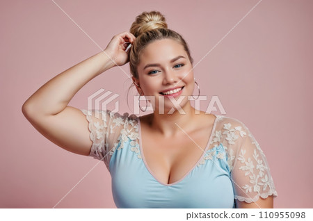 A woman with blonde hair tied in a bun, wearing a blue shirt with white lace details. She has hoop earrings and is smiling. Self-acceptance and body positivity concept. A woman with blonde hair tied in a bun, wearing a blue shirt with white lace details. She has hoop earrings and is smiling. Self-acceptance and body positivity concept. 110955098