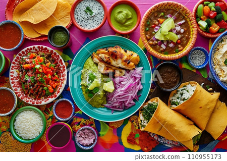 A colorful and appetizing top view of Mexican festive food for Independence Day, featuring chili, cilantro, tacos, burritos, chalupas, pozole, tamales, and chicken with mole poblano sauce. 110955173