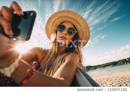 A woman wearing a hat and sunglasses sits on a bench, taking a selfie with her phone. 110955188