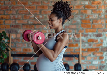 A pregnant woman lifting weights in a home gym. 110955217