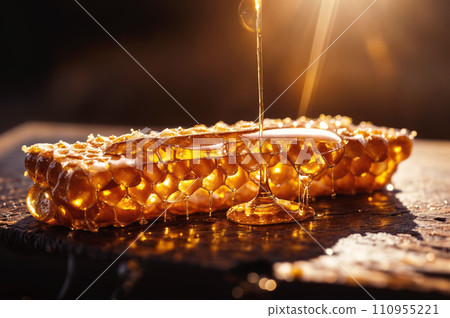 A piece of honeycomb on a wooden surface with honey dripping down. 110955221