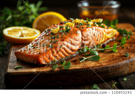 A wooden cutting board with a grilled salmon filet topped with herbs and lemon slices. A wooden cutting board with a grilled salmon filet topped with herbs and lemon slices. 110955243