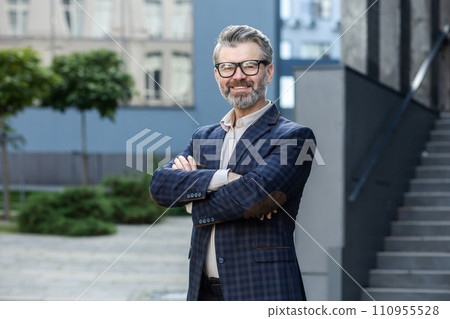 Professional senior man in business attire smiling confidently outdoors, with office backdrop, portraying success. Professional senior man in business attire smiling confidently outdoors, with office backdrop, portraying success. 110955528