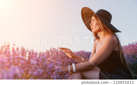 Woman lavender field. Happy carefree woman in black dress and hat with large brim walking in a lavender field during sunset. Perfect for inspirational and warm concepts in travel and wanderlust. Woman lavender field. Happy carefree woman in black dress and hat with large brim walking in a lavender field during sunset. Perfect for inspirational and warm concepts in travel and wanderlust. 110955813