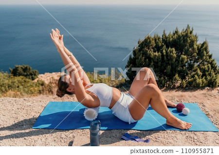 Woman sea pilates. Sporty happy middle aged woman practicing fitness on yoga mat with balls and roller near sea, smiling active female outside, enjoying healthy lifestyle, harmony and meditation. Woman sea pilates. Sporty happy middle aged woman practicing fitness on yoga mat with balls and roller near sea, smiling active female outside, enjoying healthy lifestyle, harmony and meditation. 110955871