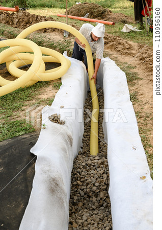 A worker carries a yellow perforated drainage pipe. Groundwater drainage works in the field 110956160