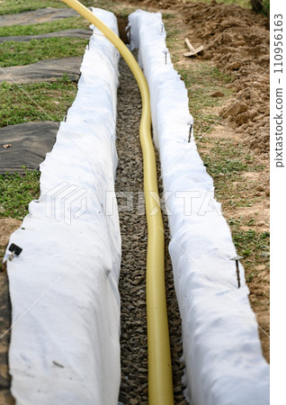 Yellow corrugated pipe with perforation in a trench with crushed stone and geotextile. Drainage works for the removal of ground water. Yellow corrugated pipe with perforation in a trench with crushed stone and geotextile. Drainage works for the removal of ground water. 110956163