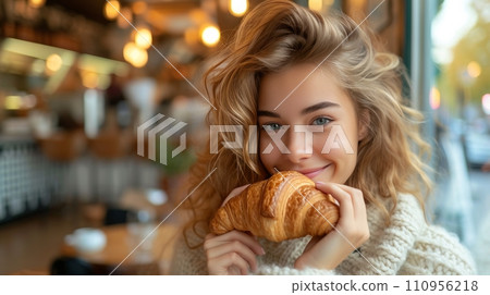 Young beautiful girl eating a large croissant in a Parisian cafe 110956218