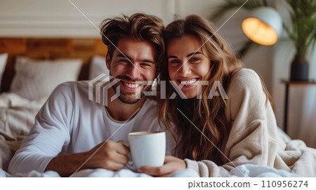 Young and happy couple in pajamas drinking coffee in bed Young and happy couple in pajamas drinking coffee in bed 110956274