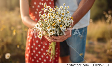 A man in denim shorts and a T-shirt gives a bouquet of daisies to a girl wearing a red polka dot sundress 110957181