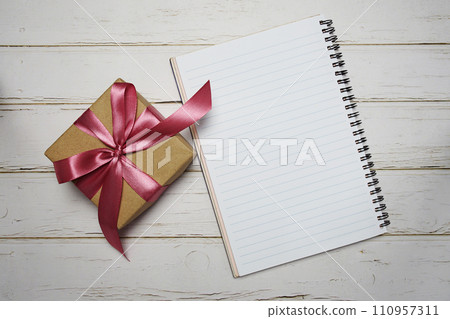 Empty Notebook and Gift box with pink ribbon on wooden background 110957311