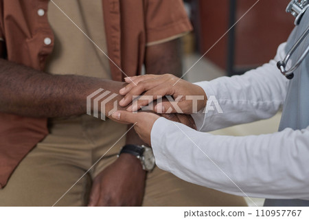 Unrecognizable female medical worker holding hand of her black patient expressing her moral support 110957767