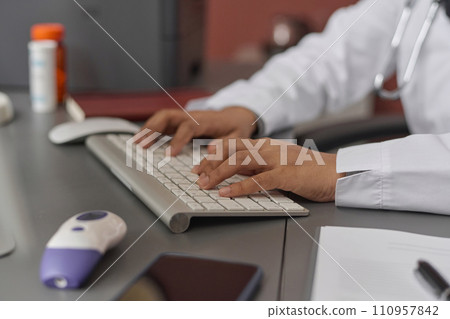 Hands of unrecognizable female doctor typing on computer keyboard sitting at desk at her workplace 110957842