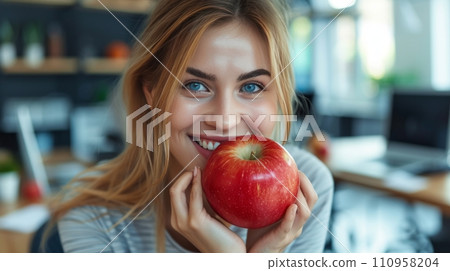 Happy woman eating big red apple sitting at computer in office Happy woman eating big red apple sitting at computer in office 110958204