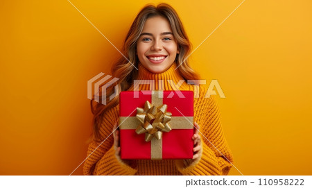Happy young beautiful girl holding a big red gift box with a golden bow on a minimalistic bright background Happy young beautiful girl holding a big red gift box with a golden bow on a minimalistic bright background 110958222