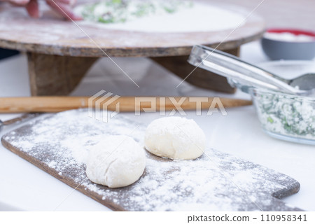Front view of dough for pita. taco lying on wooden board dusted with flour, being rolled out outdoor. Concept of cooking. 110958341