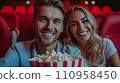 Beautiful young couple sitting in a cinema with a big bucket of popcorn 110958450