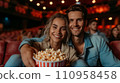 Beautiful young couple sitting in a cinema with a big bucket of popcorn 110958458