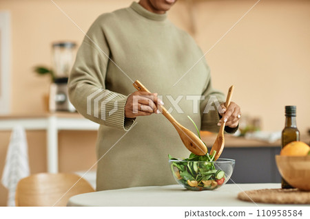 Cropped shot with focus on glass bowl with healthy vegetable salad and unrecognizable pregnant woman mixing ingredients with wooden stirring spoons Cropped shot with focus on glass bowl with healthy vegetable salad and unrecognizable pregnant woman mixing ingredients with wooden stirring spoons 110958584