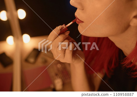 Close up shot of unrecognizable female performer putting on red lipstick in dressing mirror light backstage Close up shot of unrecognizable female performer putting on red lipstick in dressing mirror light backstage 110958887