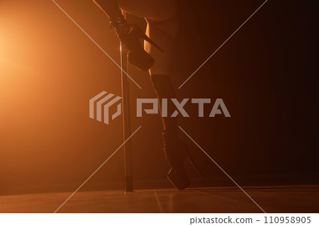 Unrecognizable female exotic dancer in black high-heeled shoes performing on stage in dark nightclub 110958905
