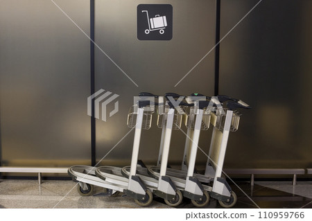 Sign on wall indicating where luggage carts are parked at the airport next to parked bag rollers Sign on wall indicating where luggage carts are parked at the airport next to parked bag rollers 110959766