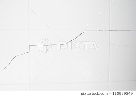 A white tiled wall with water droplets in the bathroom. Broken, cracked tiles. destroyed wall as a result of the earthquake. 110959849