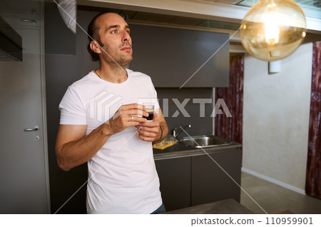 Contented young adult man holding cup of aroma arabica espresso coffee, enjoying warm beverage at home 110959901