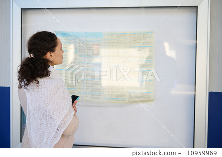 Young woman commute looking at schedules on the train platform at railway station, planning her route railway stop 110959969