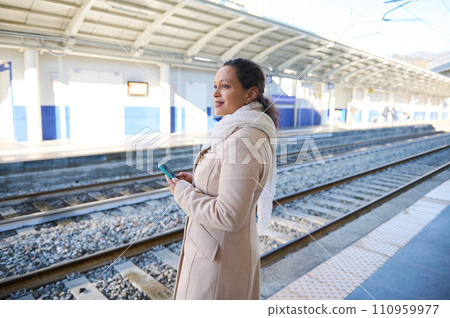 Young adult woman using smartphone while waiting high speed train at platform. Railway transport, online tickets booking 110959977