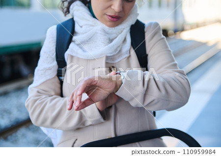 Close-up of a backpacked female passenger checking time on her wrist watch, waiting for a train on the railway station 110959984