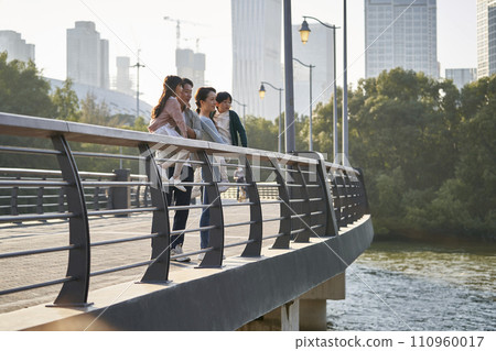 asian family with two children standing on pedestrian bridge looking at view in city park 110960017