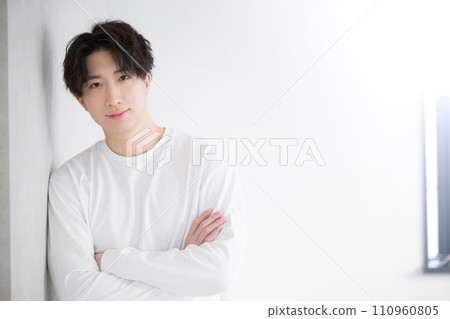 Young handsome man leaning against a wall and folding his arms Young handsome man leaning against a wall and folding his arms 110960805