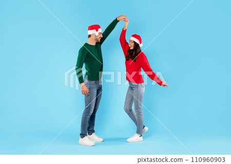 couple in Santa hats dancing celebrating Christmas on blue backdrop 110960903