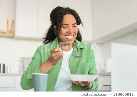 Black Woman Watching Videos On Laptop Eating Breakfast In Kitchen 110960911