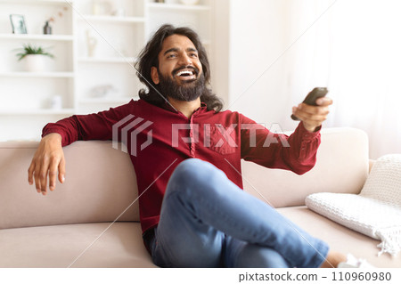Emotional indian man watching TV at home, laughing 110960980
