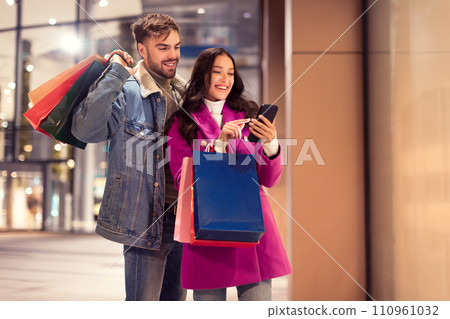 European couple enjoying online shopping on smartphone standing near mall European couple enjoying online shopping on smartphone standing near mall 110961032