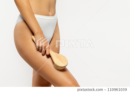 Slim caucasian young lady in underwear doing anti-cellulite massage with natural wooden brush 110961039