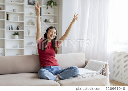 Carefree Young Asian Woman In Wireless Headphones Listening Music At Home Carefree Young Asian Woman In Wireless Headphones Listening Music At Home 110961048