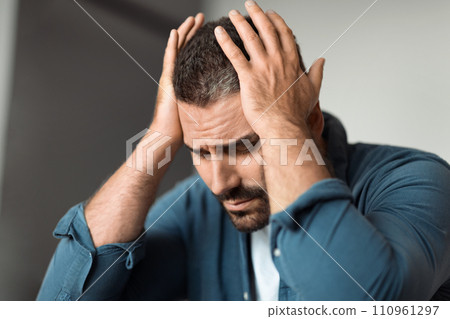 Frustrated man in grief holding head in hands at home Frustrated man in grief holding head in hands at home 110961297