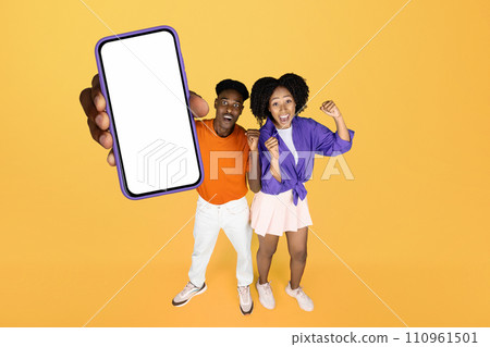 Black couple showing large mobile phone against yellow studio backdrop Black couple showing large mobile phone against yellow studio backdrop 110961501