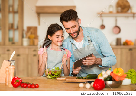 Father and daughter looking at tablet while cooking in kitchen 110961555