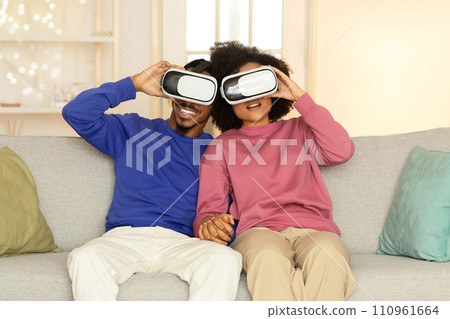 African American spouses wearing virtual reality headsets in living room 110961664