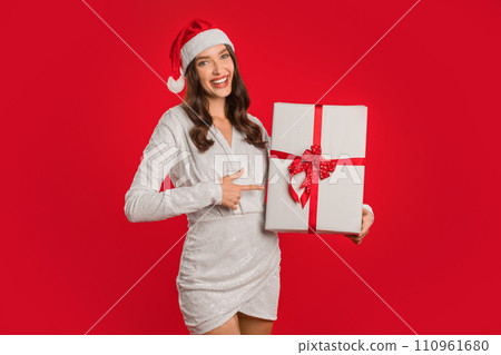 Joyful woman celebrates Christmas season pointing at wrapped gift, studio 110961680
