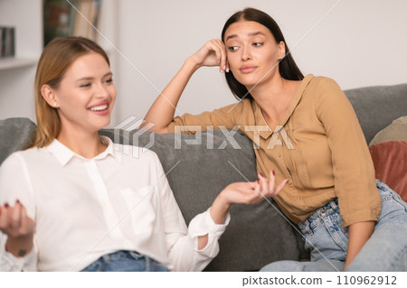 Jealous Lady Listening To Her Cheerful Friend Talking At Home 110962912