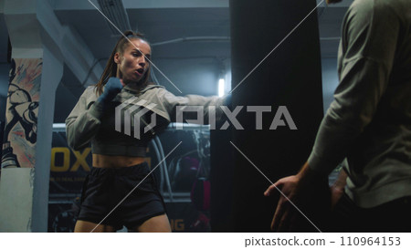Female fighter in boxing bandages exercises with male trainer 110964153