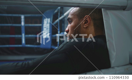 Fighter with beads of sweat on face rests in boxing ring corner Fighter with beads of sweat on face rests in boxing ring corner 110964330